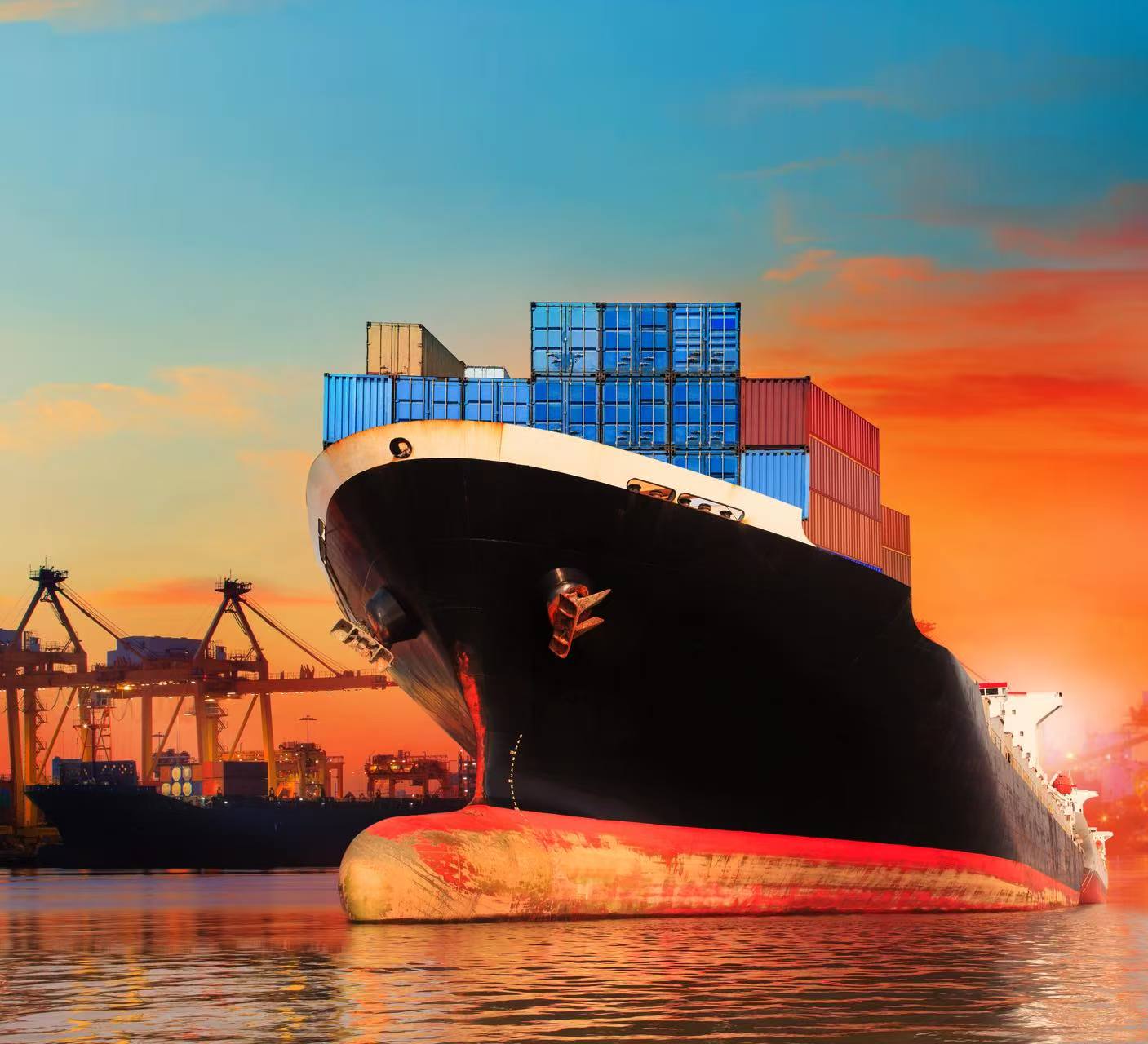 Container vessel alongside port cranes at sunset